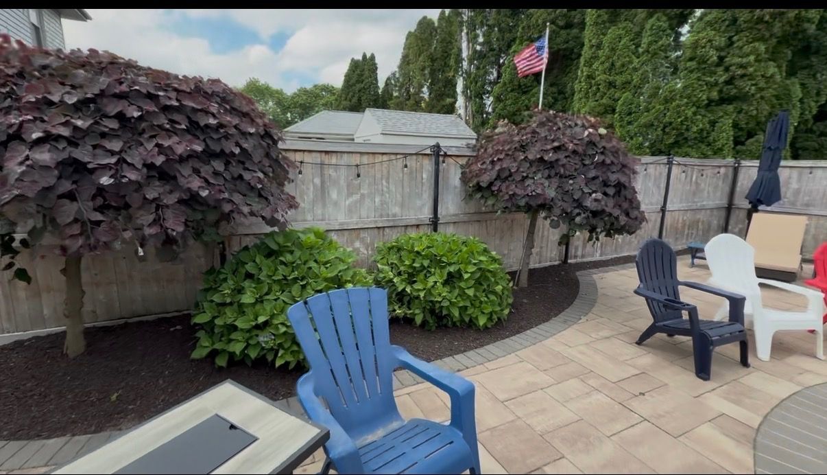 Installed paver patio with Adirondack chairs, weeping trees, and hydrangea beds in a Rhode Island backyard